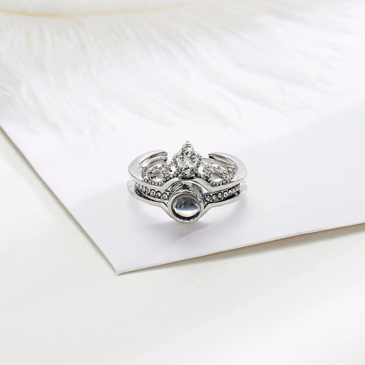 Anel feminino de prata com aro ajustável, pedra central e acabamento em formato de coroa com detalhes cravejados.