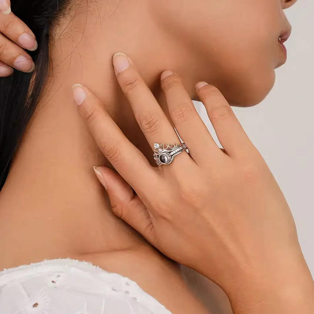 Anel feminino de prata personalizado com foto, visto na mão que esta próxima ao pescoço de uma mulher, destacando o design delicado com coroa e pedra central.