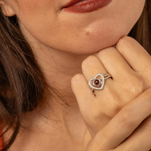 Anel feminino de prata com coração e foto personalizada usado no dedo, em close na mão.