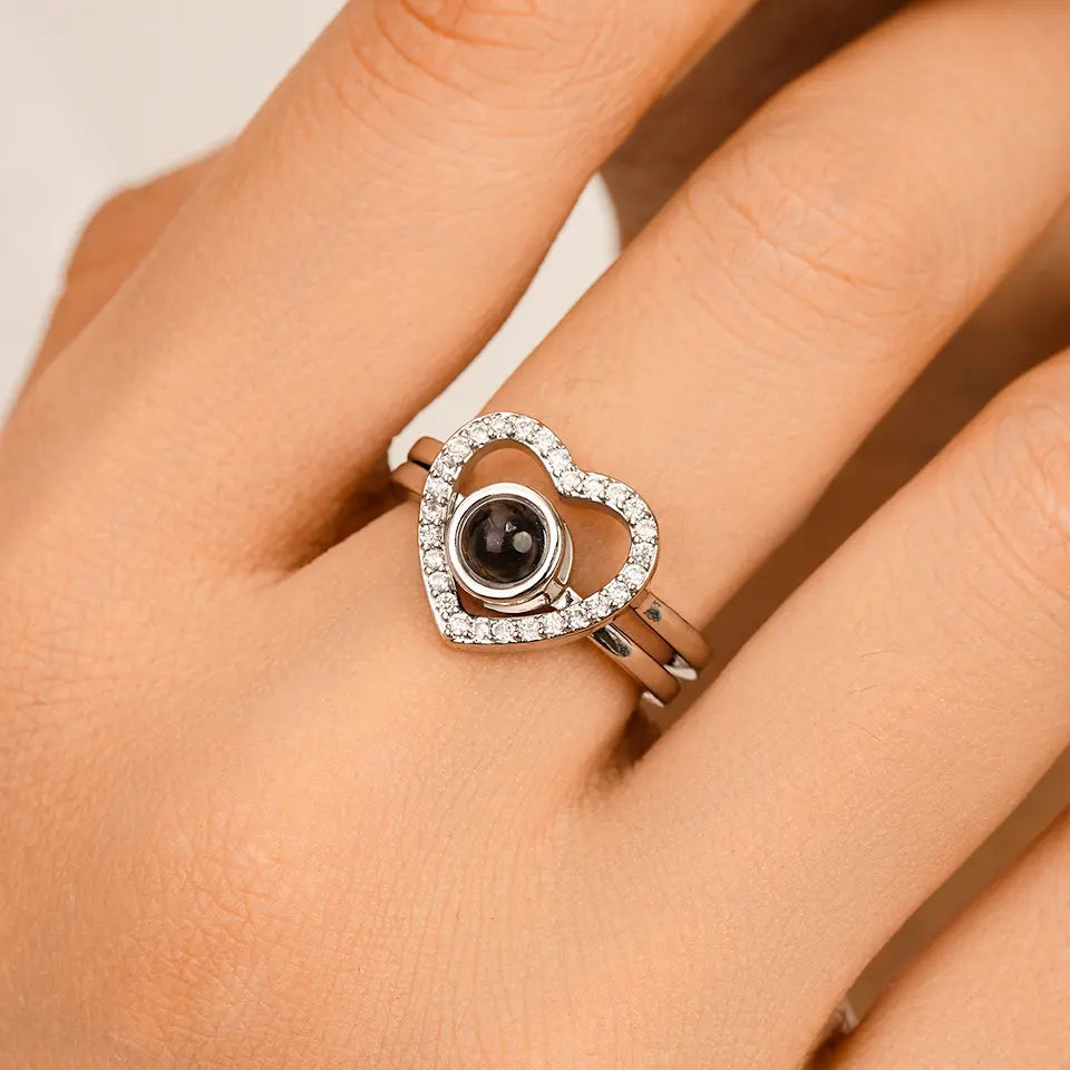 Anel feminino de prata com formato de coração e pedra central preta para foto personalizada sendo usado no dedo, com acabamento cravejado brilhante.