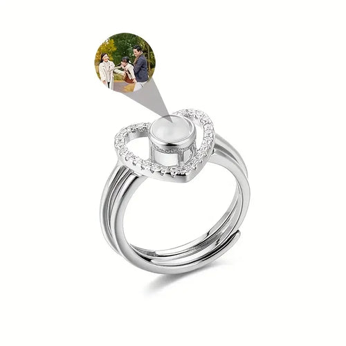 Anel feminino de prata com coração personalizado e espaço para foto, em fundo branco com exemplo de imagem de casal no topo.