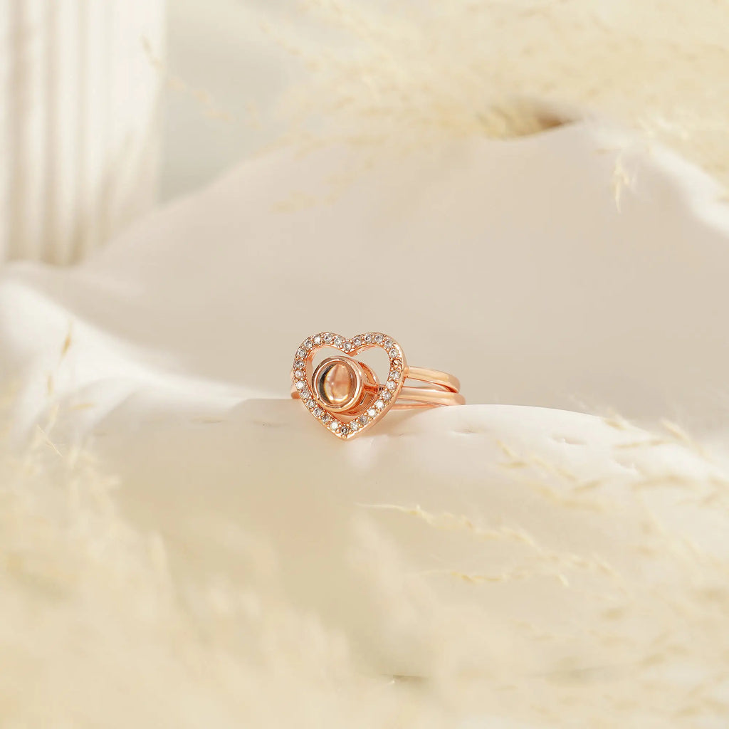 Anel feminino rosé personalizado com coração cravejado e miniatura de foto, fotografado sobre fundo bege.