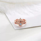 Anel feminino rosé com detalhe de coroa e pedra central, mostrado em close sobre fundo claro.