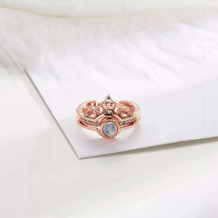 Anel feminino rosé com detalhe de coroa e pedra central, mostrado em close sobre fundo claro.