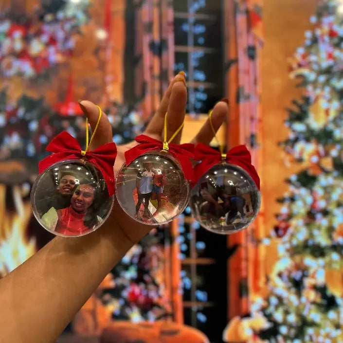 Bolas para árvore de Natal personalizadas com fotos, seguradas na mão e decoradas com laços vermelhos.