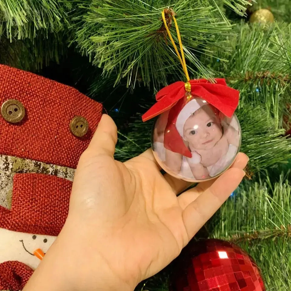 Bola de árvore de Natal personalizada com foto de bebê, segurada na mão em frente à decoração natalina.