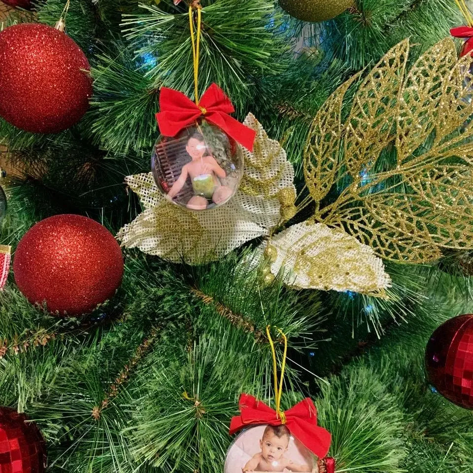 Bola de Natal personalizada com foto de criança pendurada na árvore, ao lado de enfeites vermelhos e dourados.