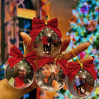 Conjunto de bolas de Natal personalizadas com fotos, exibidas na mão com laços vermelhos e fundo natalino desfocado.