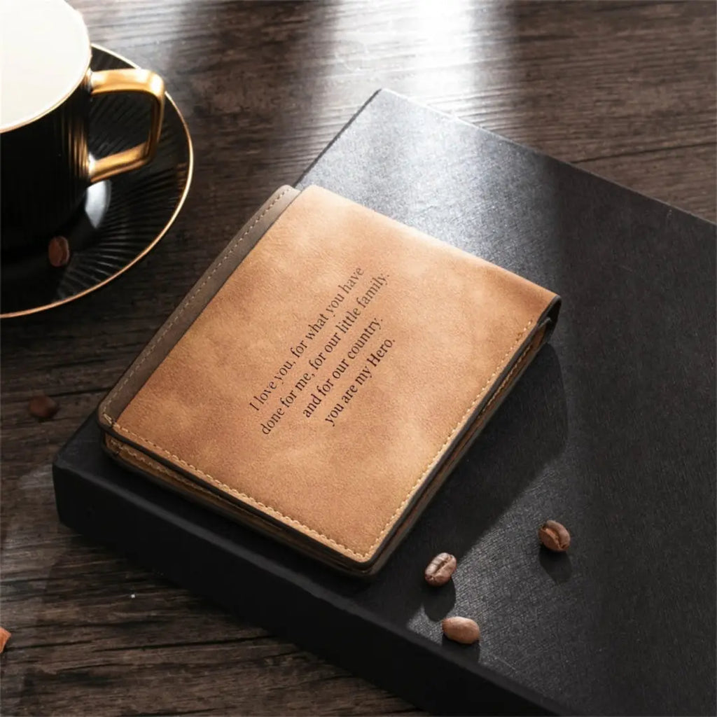Carteira de couro masculina marrom claro personalizada com frase gravada, apoiada sobre caixa preta e mesa de madeira.