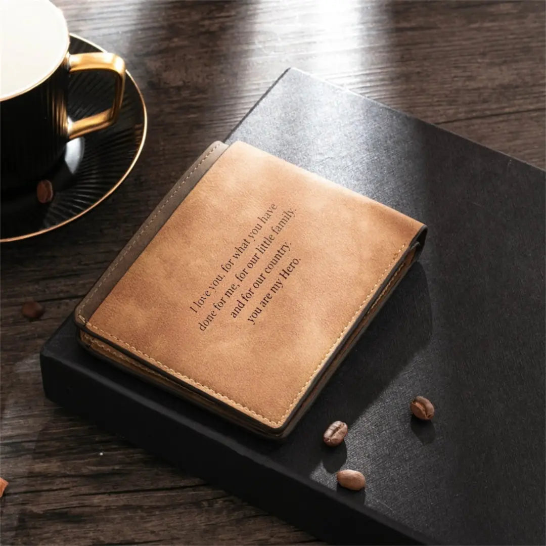Carteira de couro masculina marrom claro personalizada com frase gravada, apoiada sobre caixa preta e mesa de madeira.