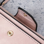Detalhe da carteira feminina rosa em couro, com costura, acabamento preto nas bordas e fecho de metal dourado.