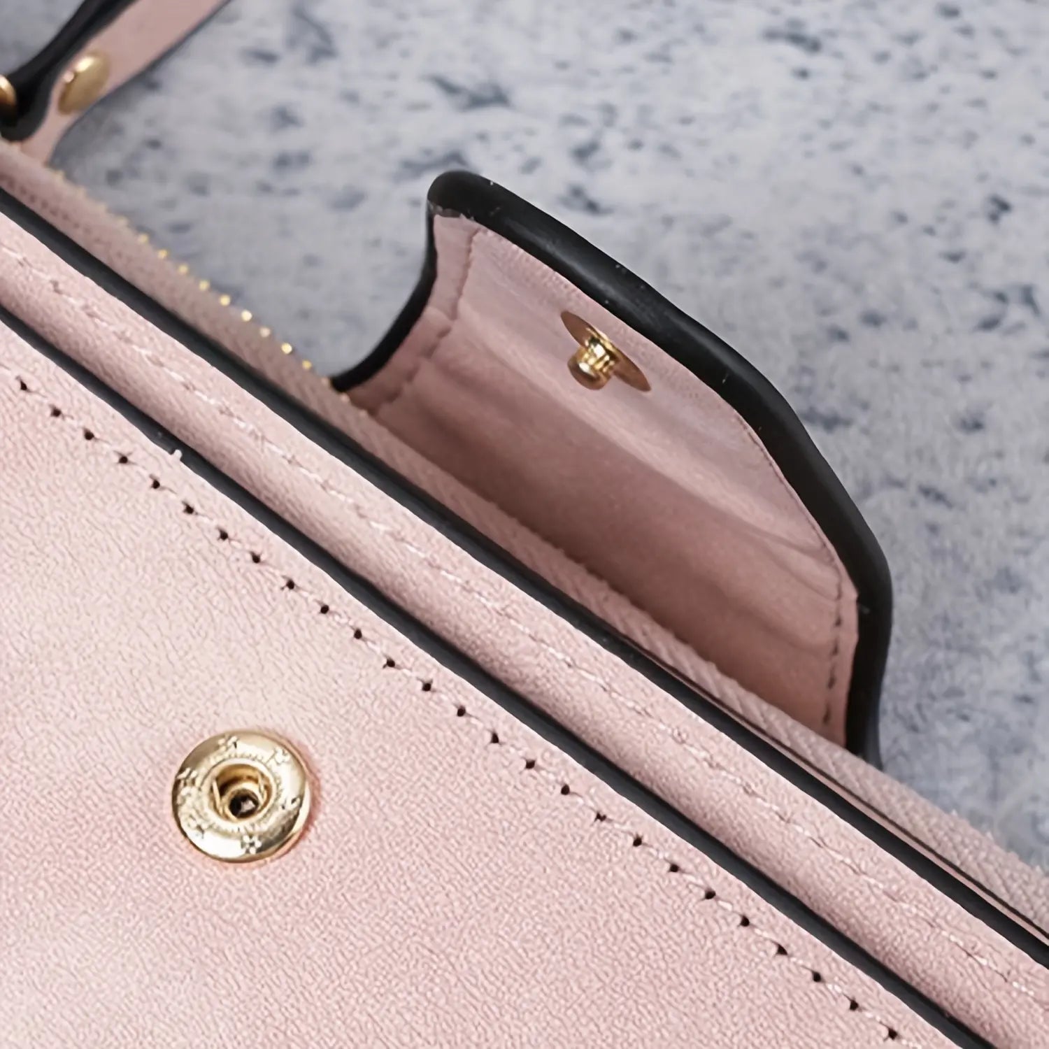Detalhe da carteira feminina rosa em couro, com costura, acabamento preto nas bordas e fecho de metal dourado.