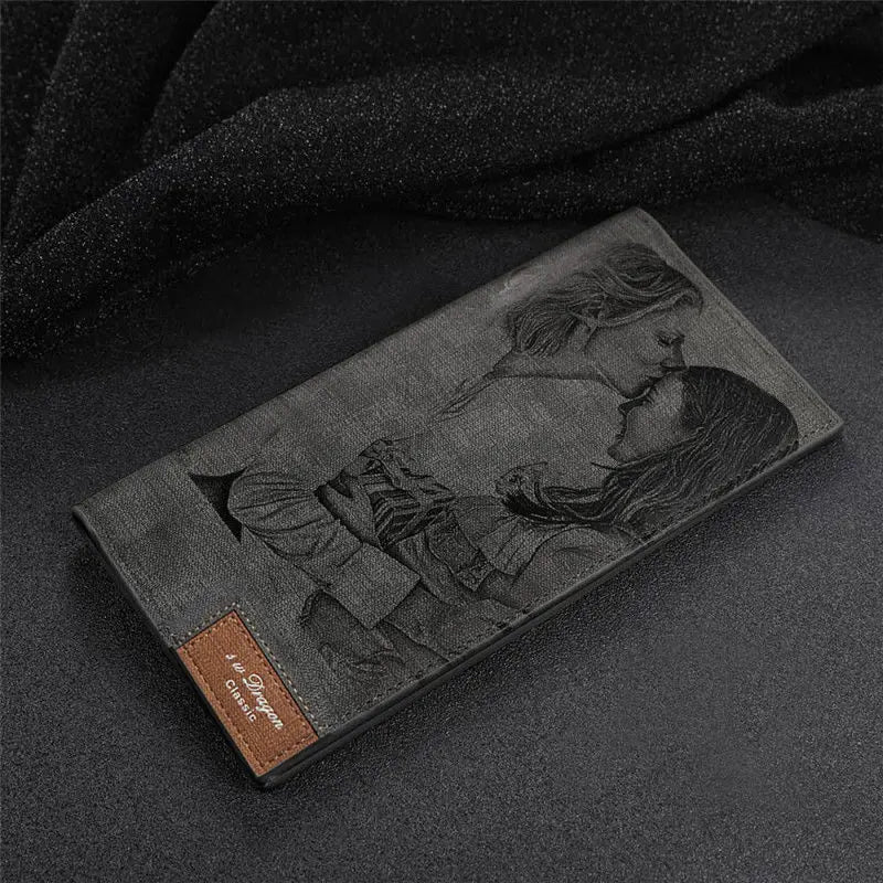 Carteira feminina cinza personalizada posicionada sobre tecido escuro, com gravação artística na frente e etiqueta marrom na base.