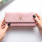 Carteira feminina rosa personalizada sendo segurada pelas mãos, com fecho frontal de pressão e detalhe decorativo dourado.