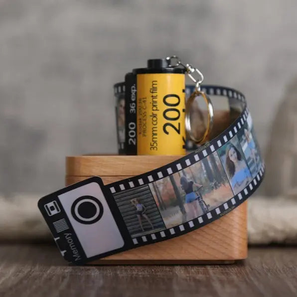 Chaveiro personalizado de câmera retrô com fita de filme decorativa exibindo pequenas fotos em destaque.