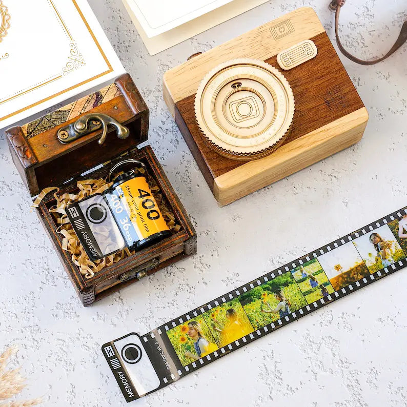 Chaveiro de câmera retrô com filme fotográfico personalizado exibido ao lado de uma caixa decorativa.