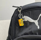 Chaveiro personalizado em formato de câmera retrô preso ao zíper de uma mochila preta.