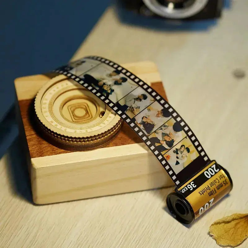 Chaveiro personalizado de câmera retrô posicionado sobre bloco de madeira com tira de filme com fotos.