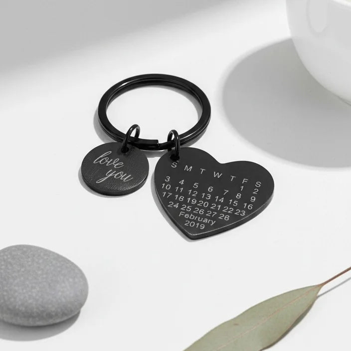 Chaveiro de coração preto personalizado posicionado sobre mesa branca com decoração minimalista ao fundo.