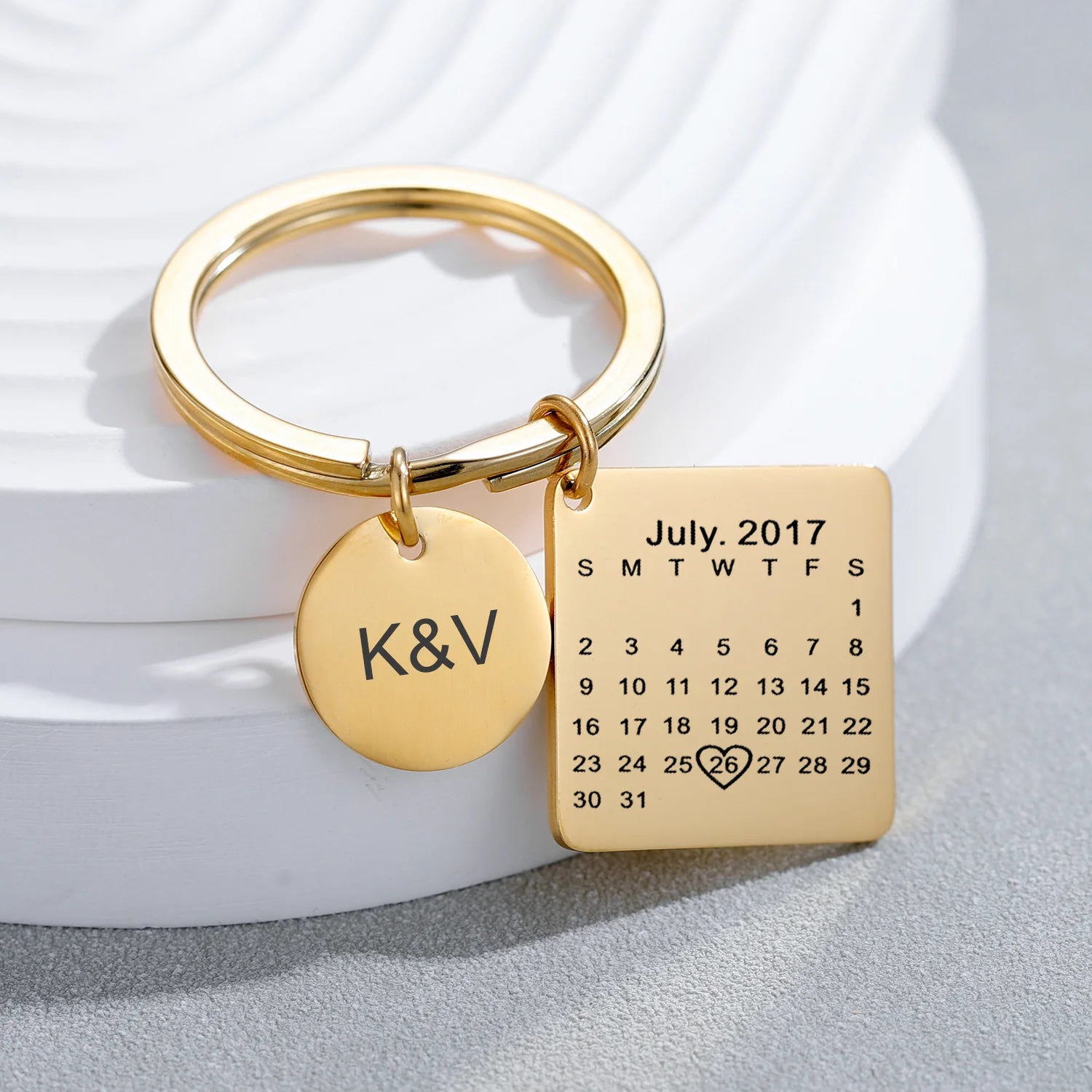 Chaveiro dourado personalizado com calendário gravado destacando data especial e pingente redondo com iniciais, em composição de apresentação de produto.