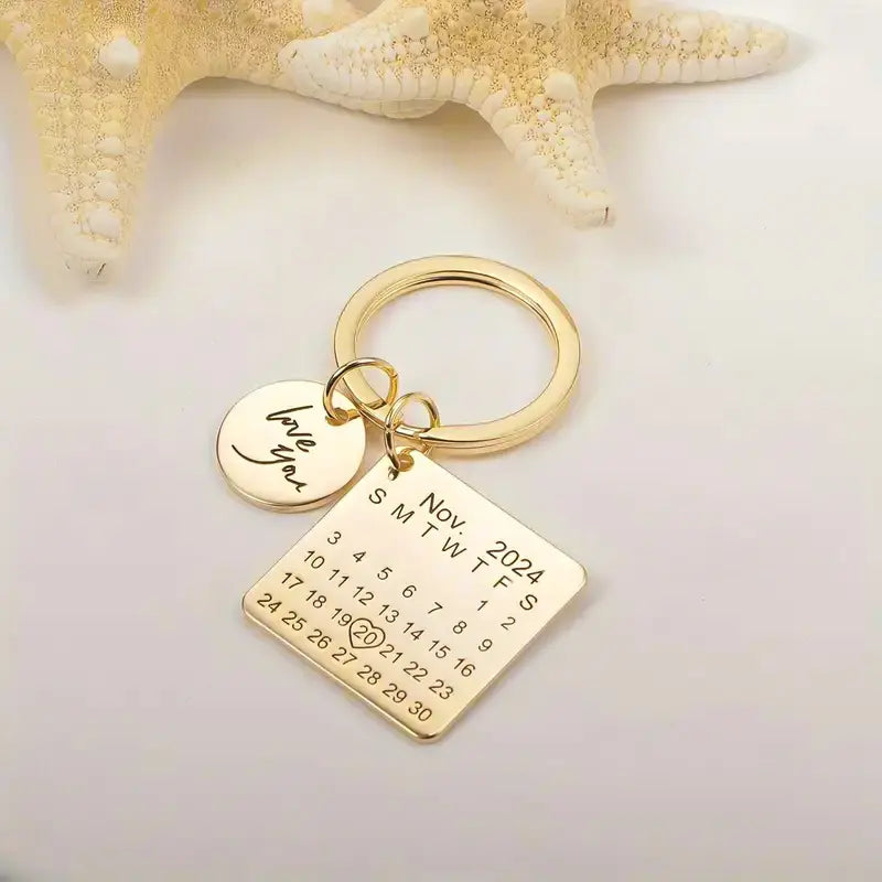Chaveiro dourado personalizado com plaquinha quadrada, disco com nome gravado e decoração com estrela do mar ao fundo.