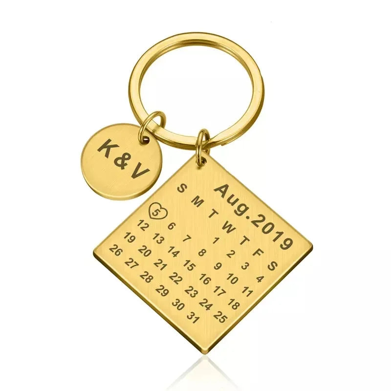 Chaveiro personalizado dourado com pingente quadrado em formato de calendário e pingente redondo com iniciais.