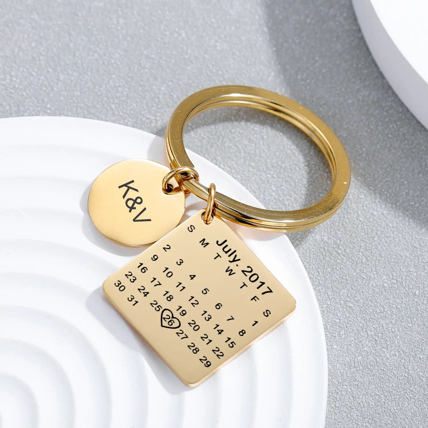 Chaveiro personalizado dourado com pingente redondo de iniciais e pingente quadrado com calendário gravado marcando data especial.