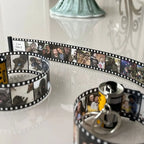 Chaveiro personalizado de câmera retrô com fita de filme exibindo várias fotos impressas.