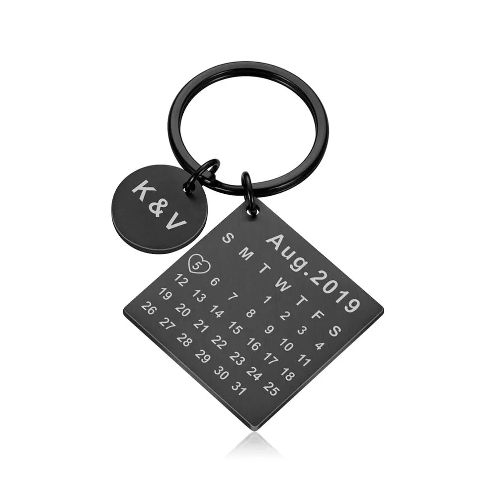 Chaveiro preto personalizado com pingente redondo com iniciais e placa quadrada com data em formato de calendário.