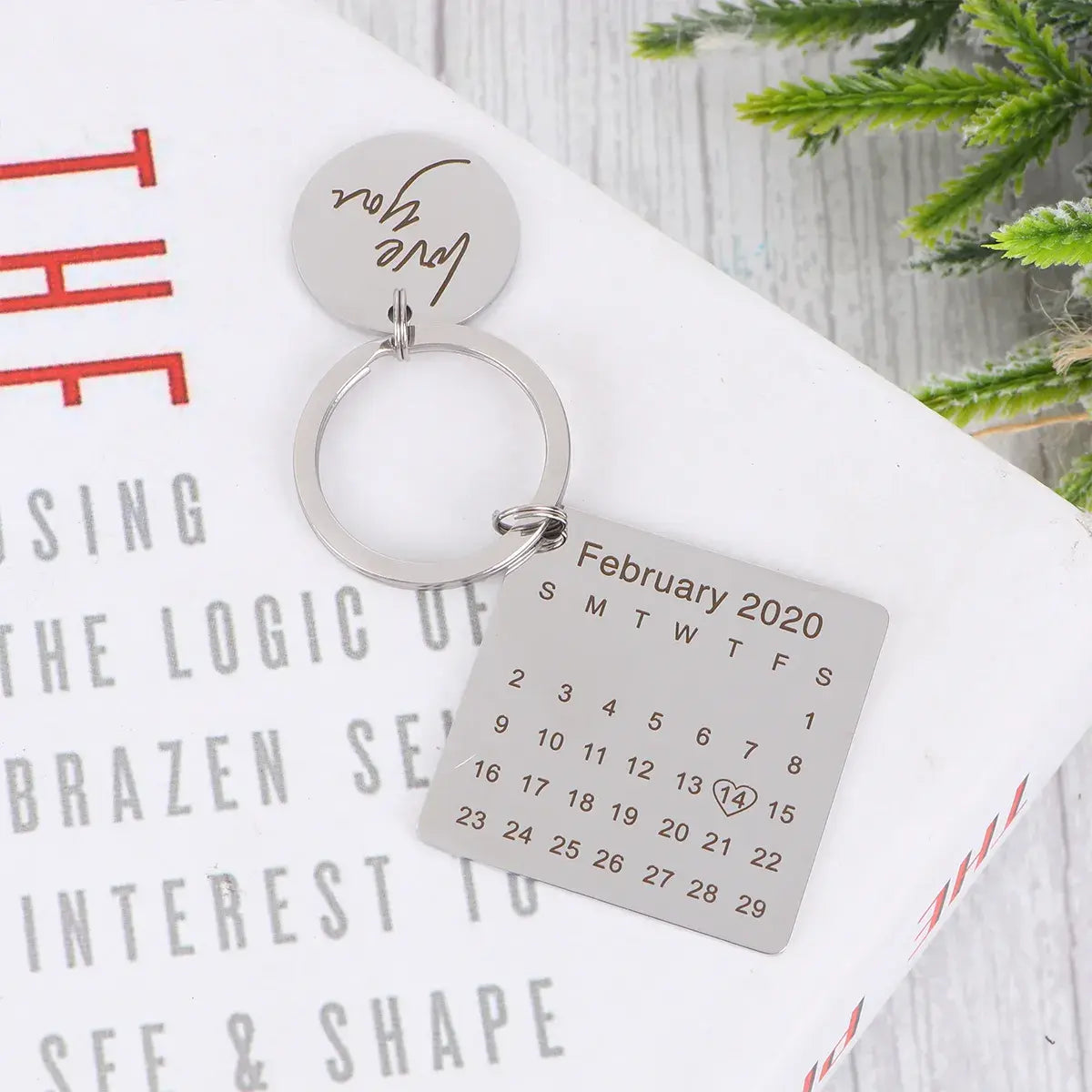 Chaveiro personalizado prateado com pingente redondo escrito 'love you' e plaquinha quadrada com calendário de fevereiro de 2020.