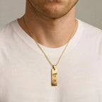 Colar dourado personalizado usado no pescoço de um homem, com pingente retangular com olhos femininos gravados no pingente pendente sobre camiseta branca.