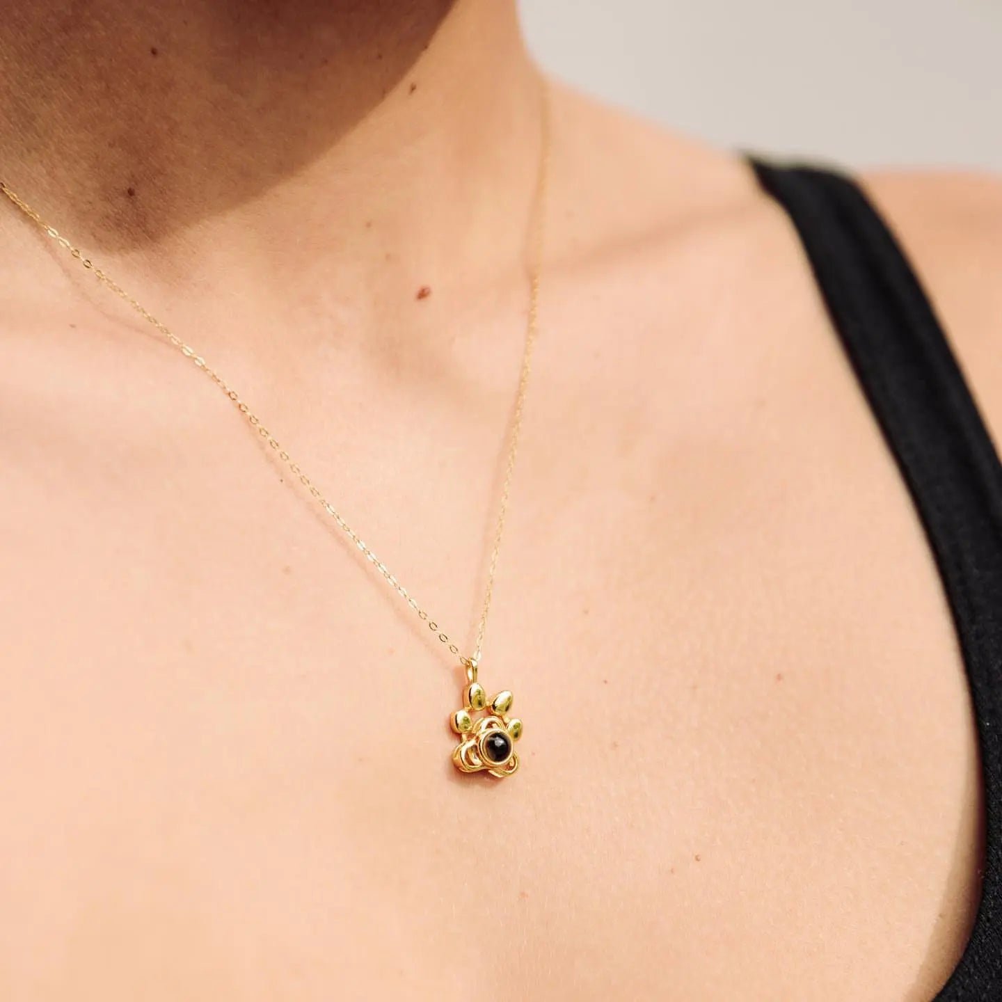 Detalhe do colar dourado personalizado com pingente de patinha sobre a pele, em visão aproximada.