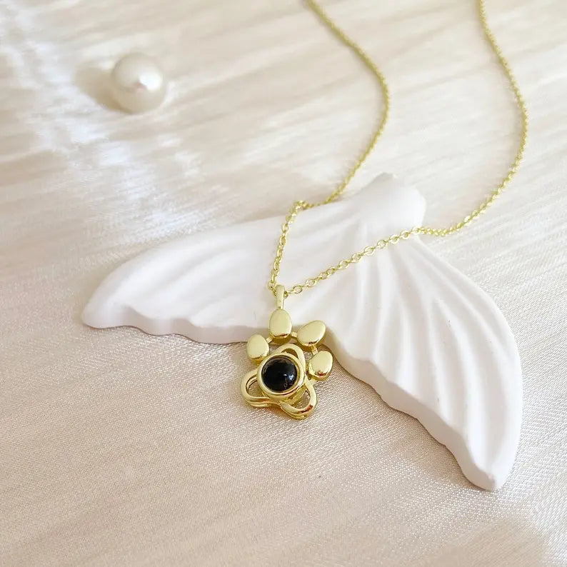 Colar dourado personalizado com pingente de patinha apoiado sobre uma concha branca, em uma composição que destaca o brilho e o formato do pingente.