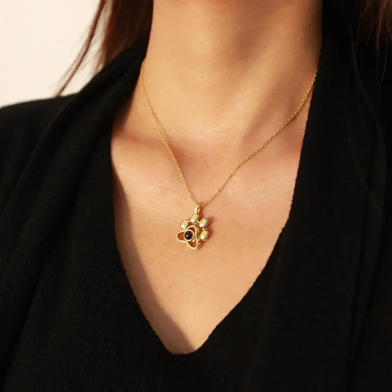 Colar dourado delicado com pingente de patinha personalizado usado sobre blusa preta.