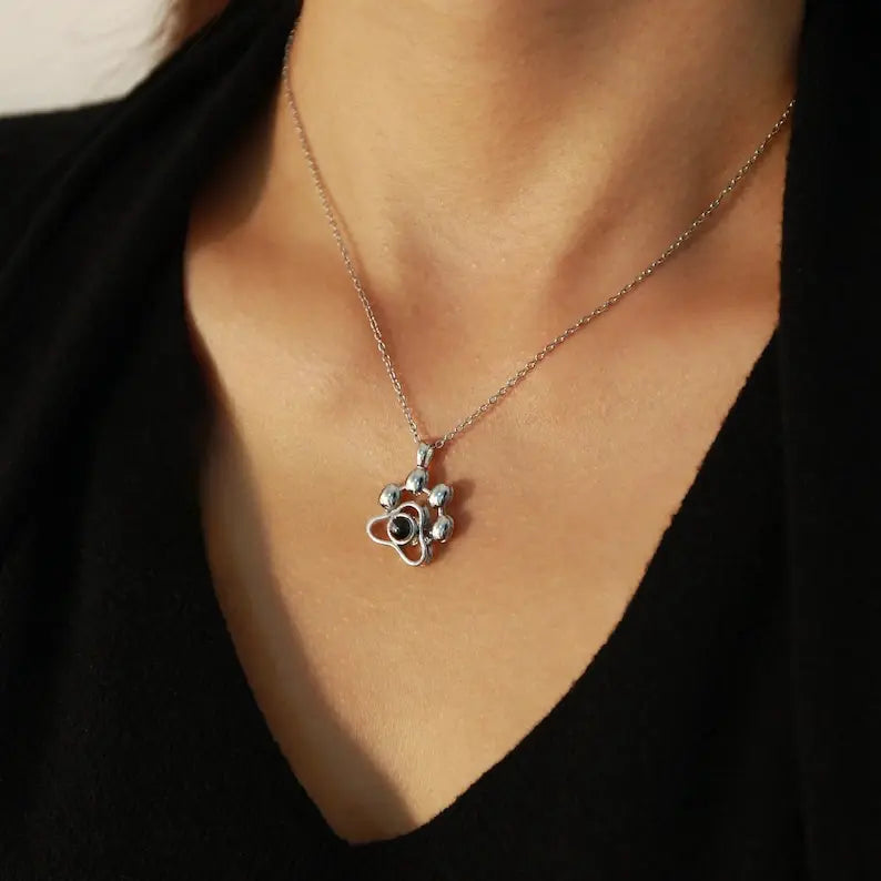 Colar personalizado de prata com pingente de patinha e foto, usado no pescoço de uma mulher.
