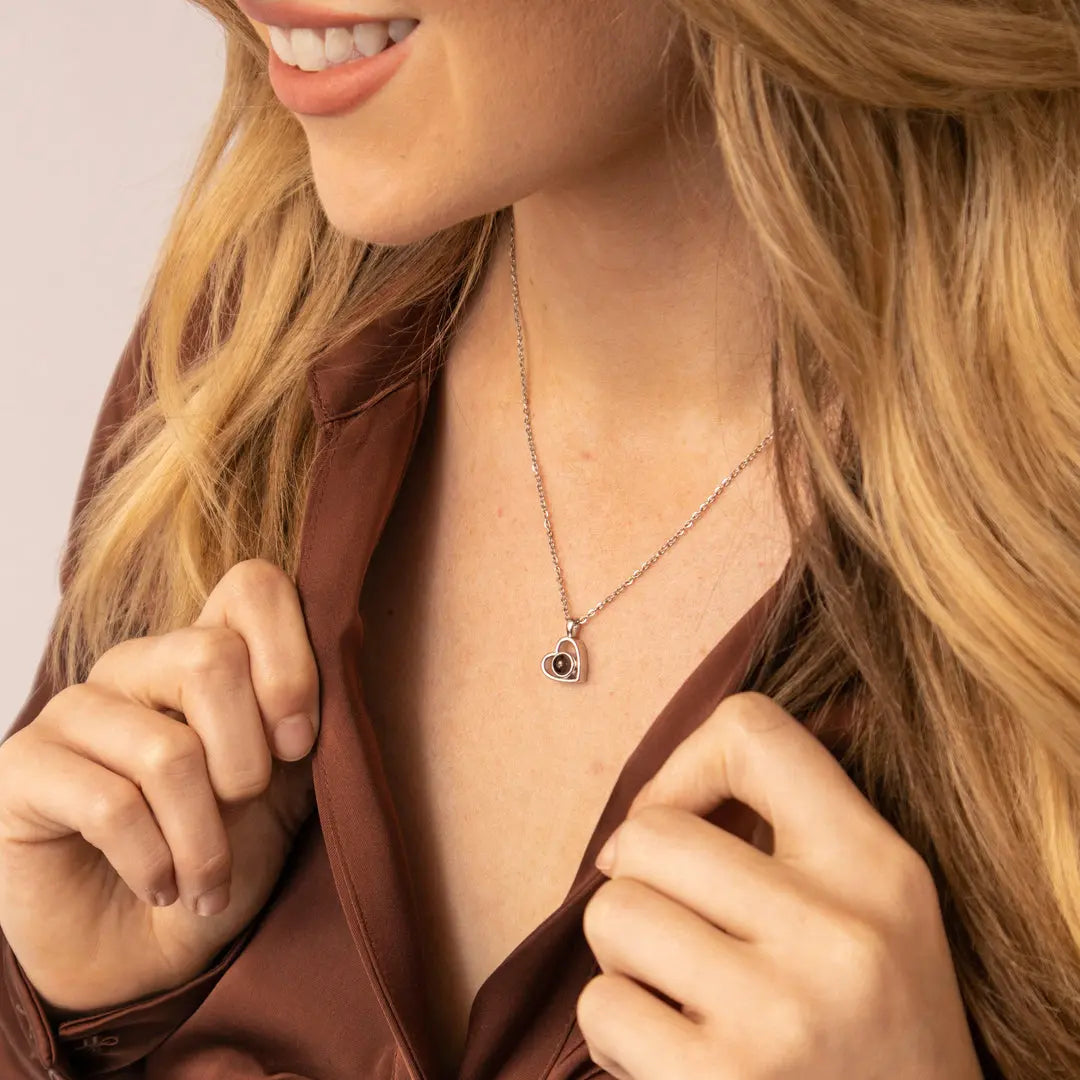 Colar personalizado com pingente de coração pequeno usado por uma mulher no decote, em foto de divulgação.