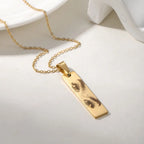 Colar personalizado dourado com pingente retangular e gravação artística de olhos, exibido sobre fundo neutro.