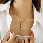 Colar personalizado dourado com pingente retangular gravado, usado no busto de uma mulher com camisa branca aberta.