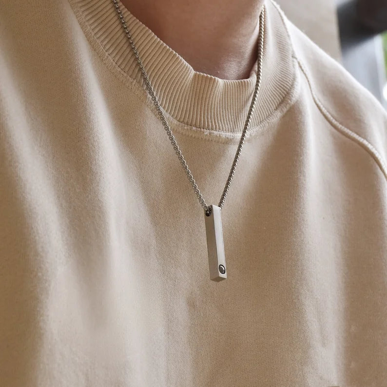 Colar personalizado masculino com pingente retangular prateado usado no pescoço sobre blusa clara.