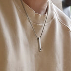 Colar personalizado masculino com pingente retangular prateado usado no pescoço sobre blusa clara.