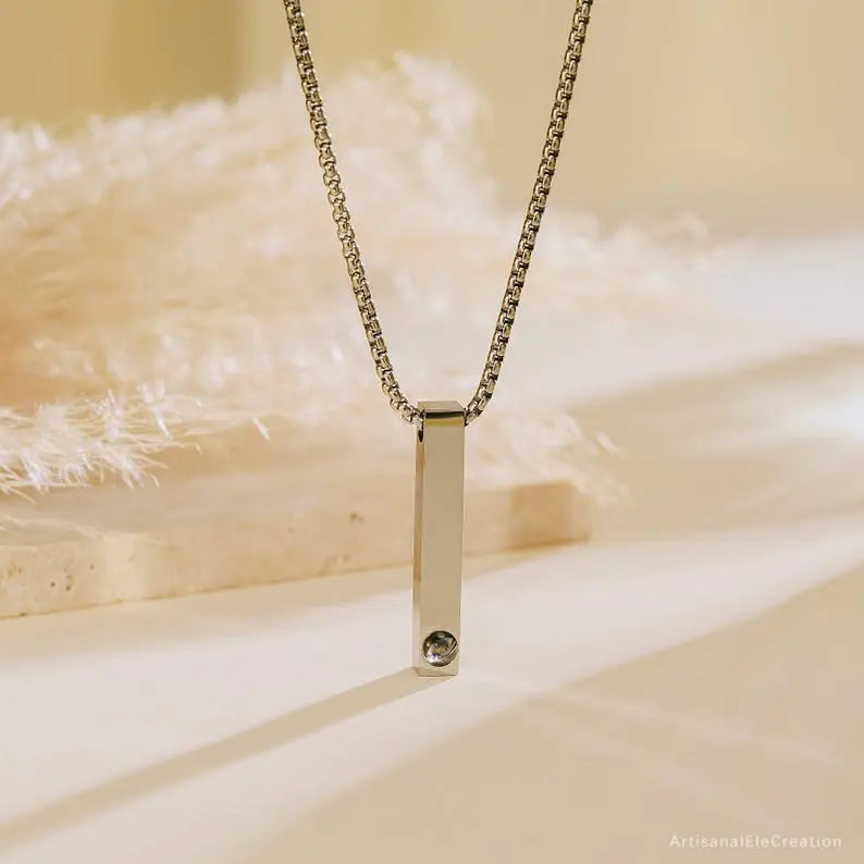 Colar personalizado com pingente retangular de prata e compartimento para foto personalizada na base, exibido pendurado em cenário suave.