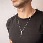 Colar de prata personalizado com pingente retangular usado com camiseta preta, mostrando o modelo no corpo masculino.