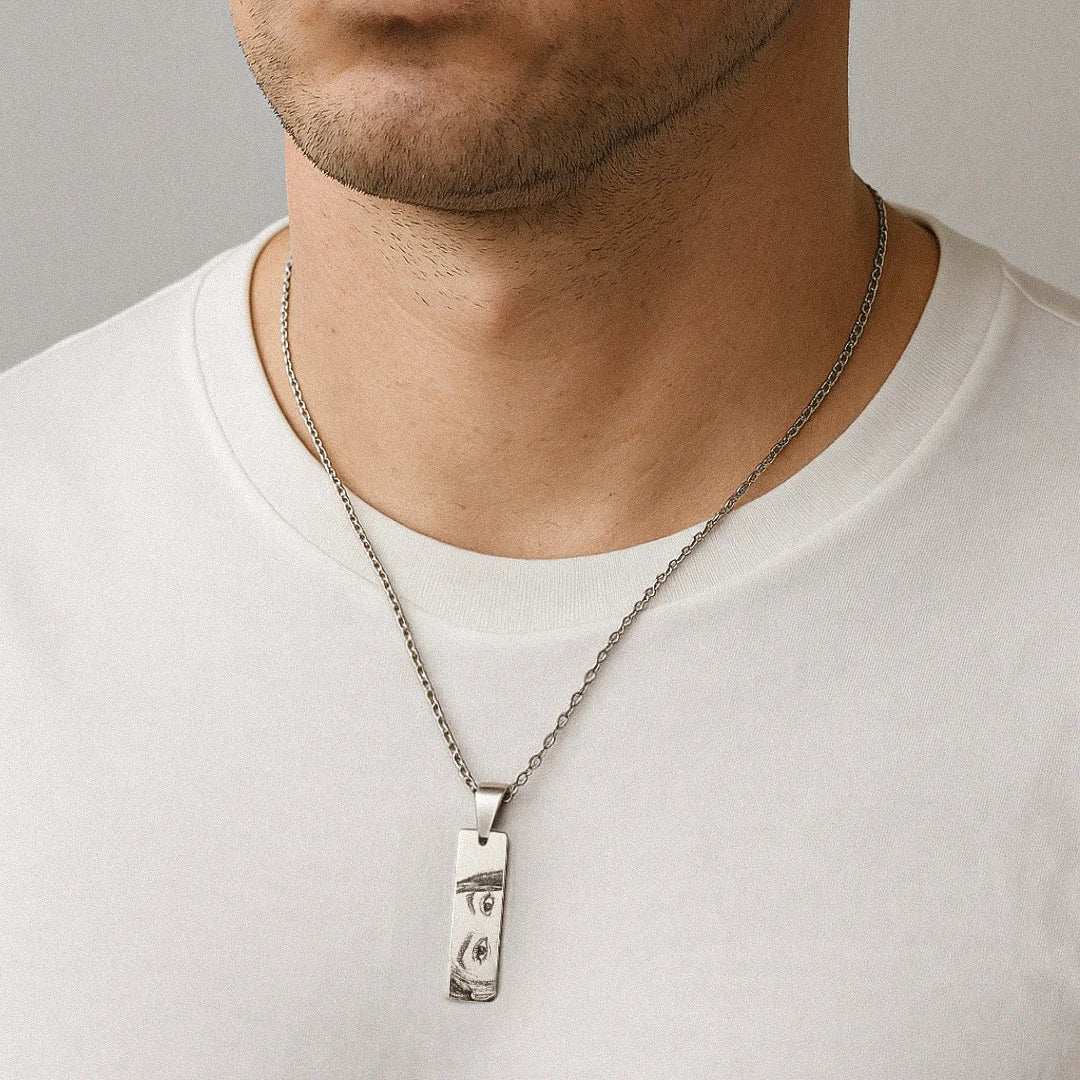 Colar personalizado de prata usado no pescoço, com pingente retangular gravado com olhos de uma mulher.