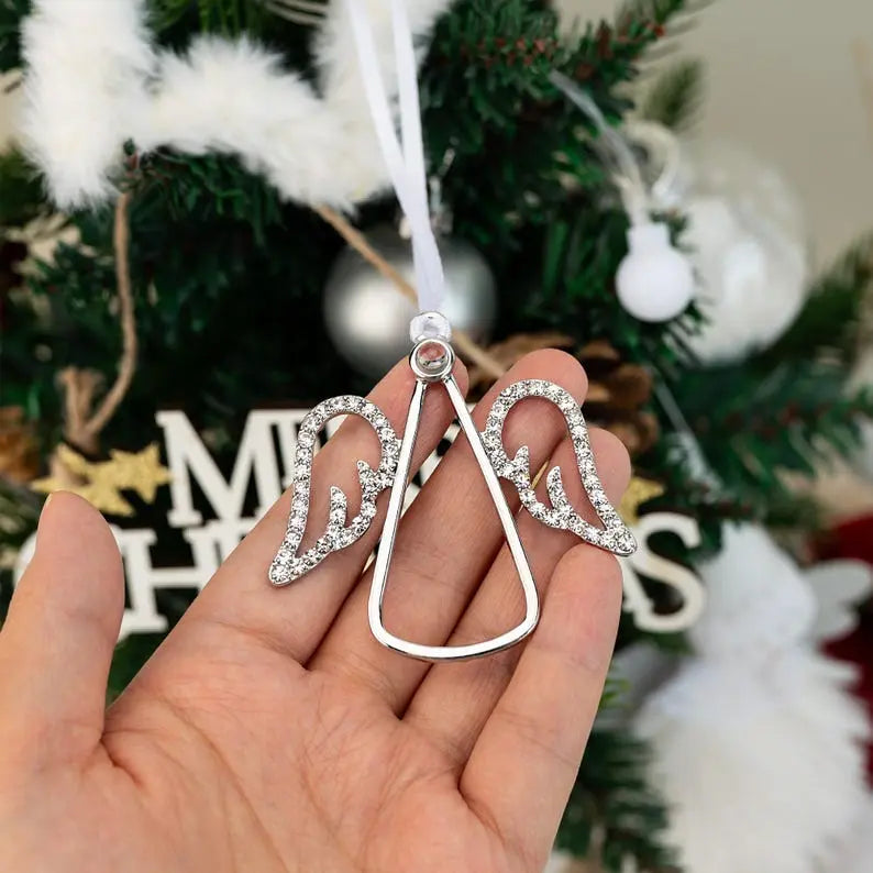 Enfeite de árvore de Natal em formato de anjo com capacidade para foto personalizada e com acabamento prateado, segurado na mão diante da decoração natalina.