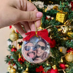 Enfeite de Natal personalizado com foto pendurado na árvore, com laço vermelho e cordão dourado.