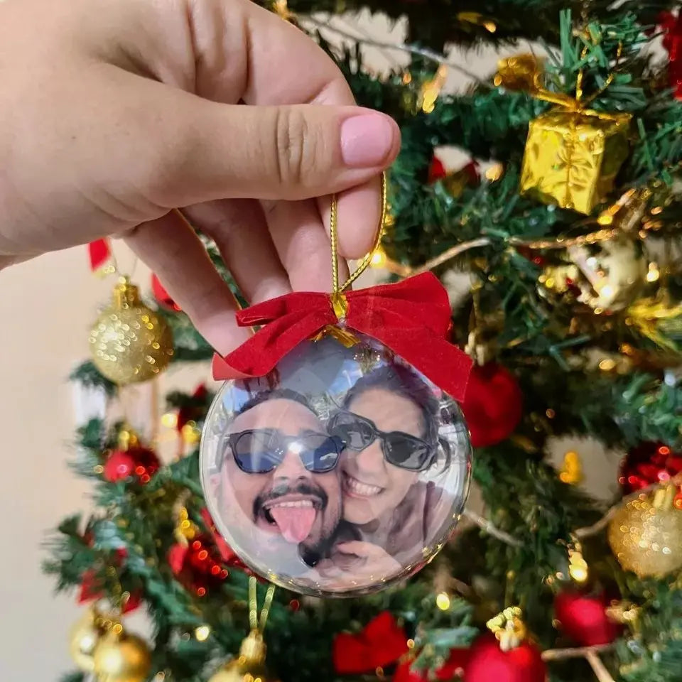 Enfeite de Natal personalizado com foto pendurado na árvore, com laço vermelho e cordão dourado.