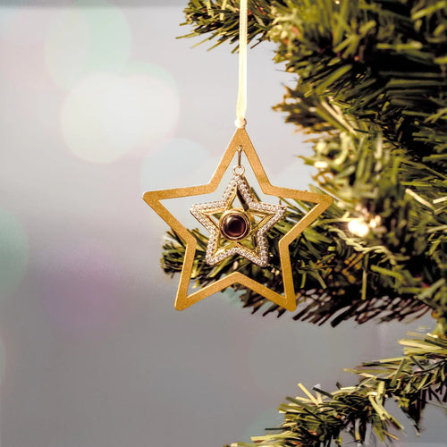 Enfeite de estrela dourada personalizada com foto pendurada na árvore de natal, com brilho decorativo ao fundo.
